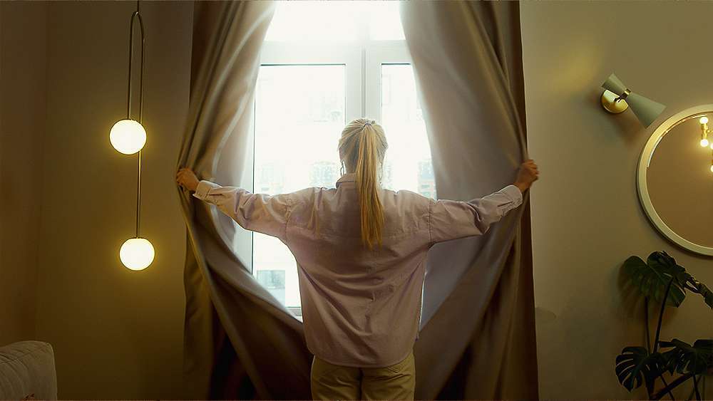 Una mujer abriendo las cortinas para que entre el sol